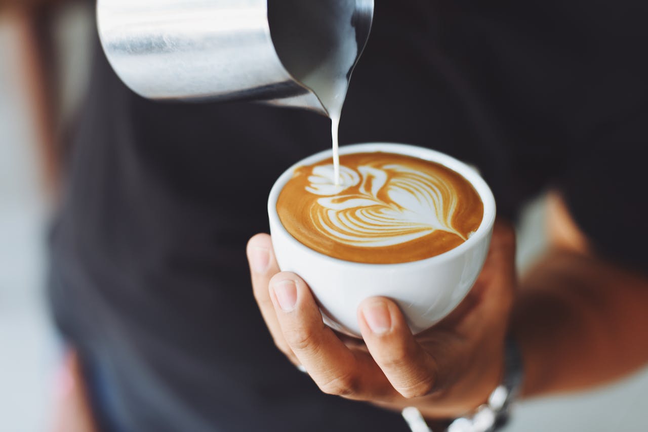 Home Close-up of a barista pouring milk to create latte art in a coffee cup.